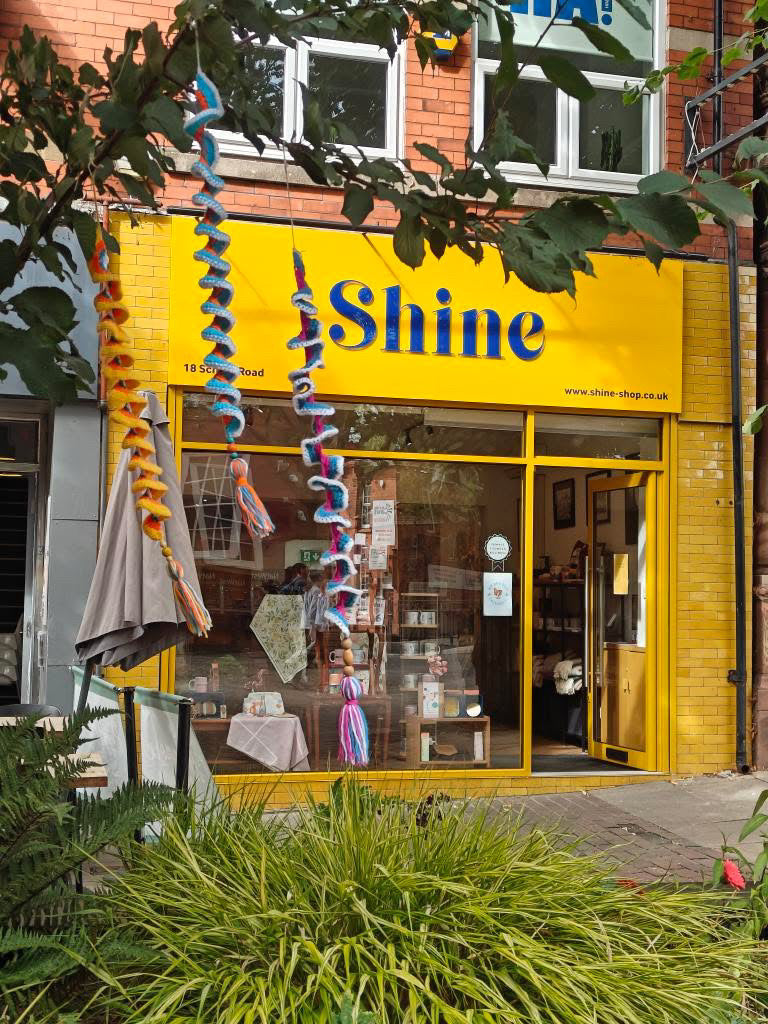Yellow storefront with 'Shine' sign and decorative ribbons on a brick building.