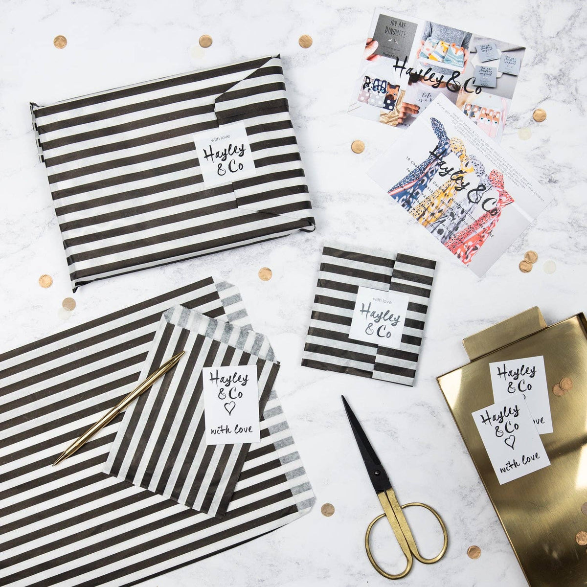 Black and white striped packages with 'Hayley & Co' on a marble surface with gold scissors.