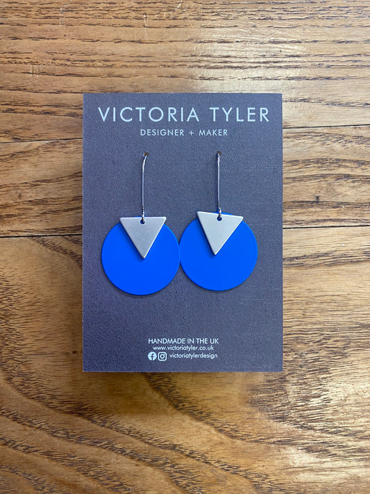 Bright Blue Circle Dangly Earrings with Silver Plate Triangles - 'Kiki'. On a black backing card which says 'Victoria Tyler, Designer + Maker 