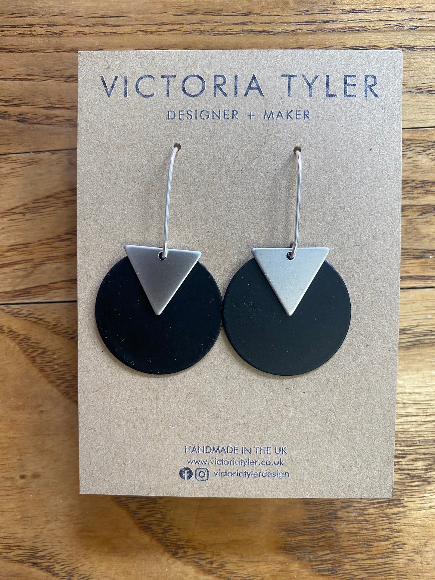 Black Circle Dangly Earrings with Silver Plate Triangles - 'Kiki'. On a black backing card which says 'Victoria Tyler, Designer + Maker