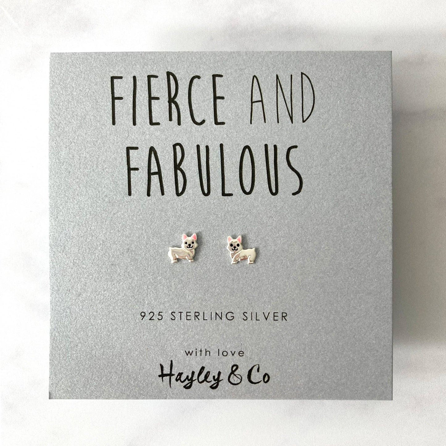A pair of sterling silver stud earrings shaped like small dogs, presented on a textured gray gift card with the brand name 'Hayley & Co' and the text 'FIERCE AND FABULOUS'.