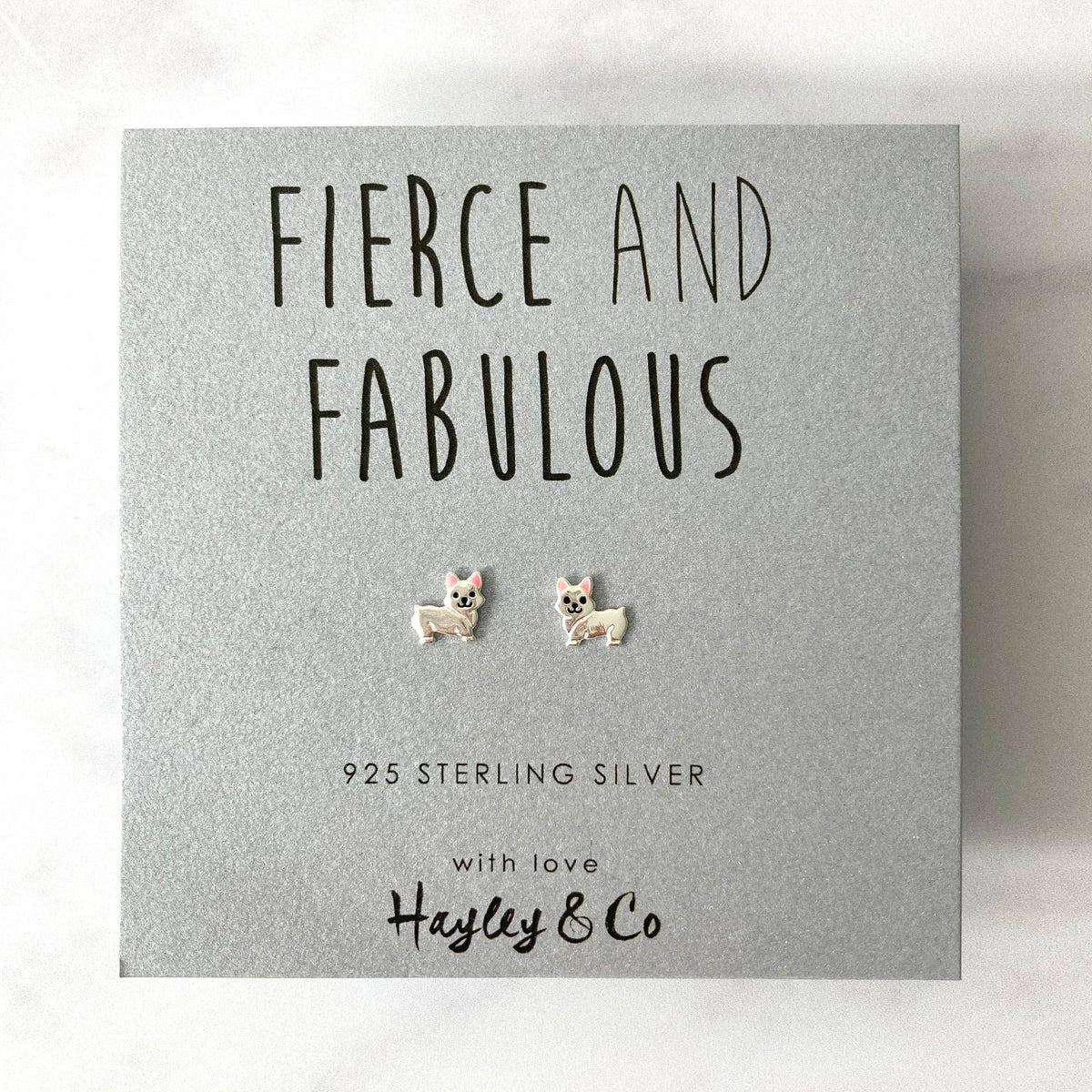 A pair of sterling silver stud earrings shaped like small dogs, presented on a textured gray gift card with the brand name 'Hayley & Co' and the text 'FIERCE AND FABULOUS'.