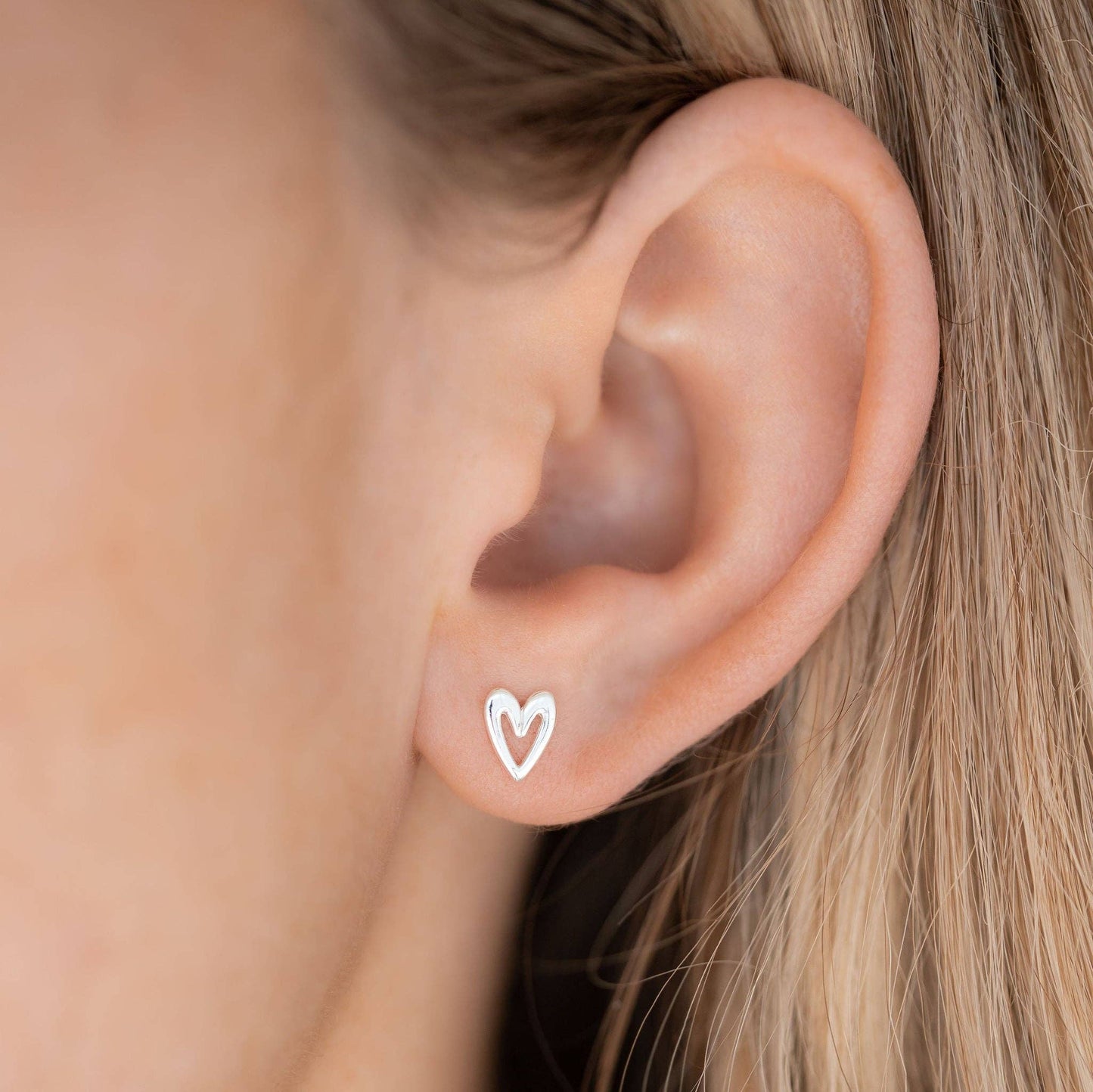 A close-up of a person's ear wearing a small silver heart-shaped stud earring.