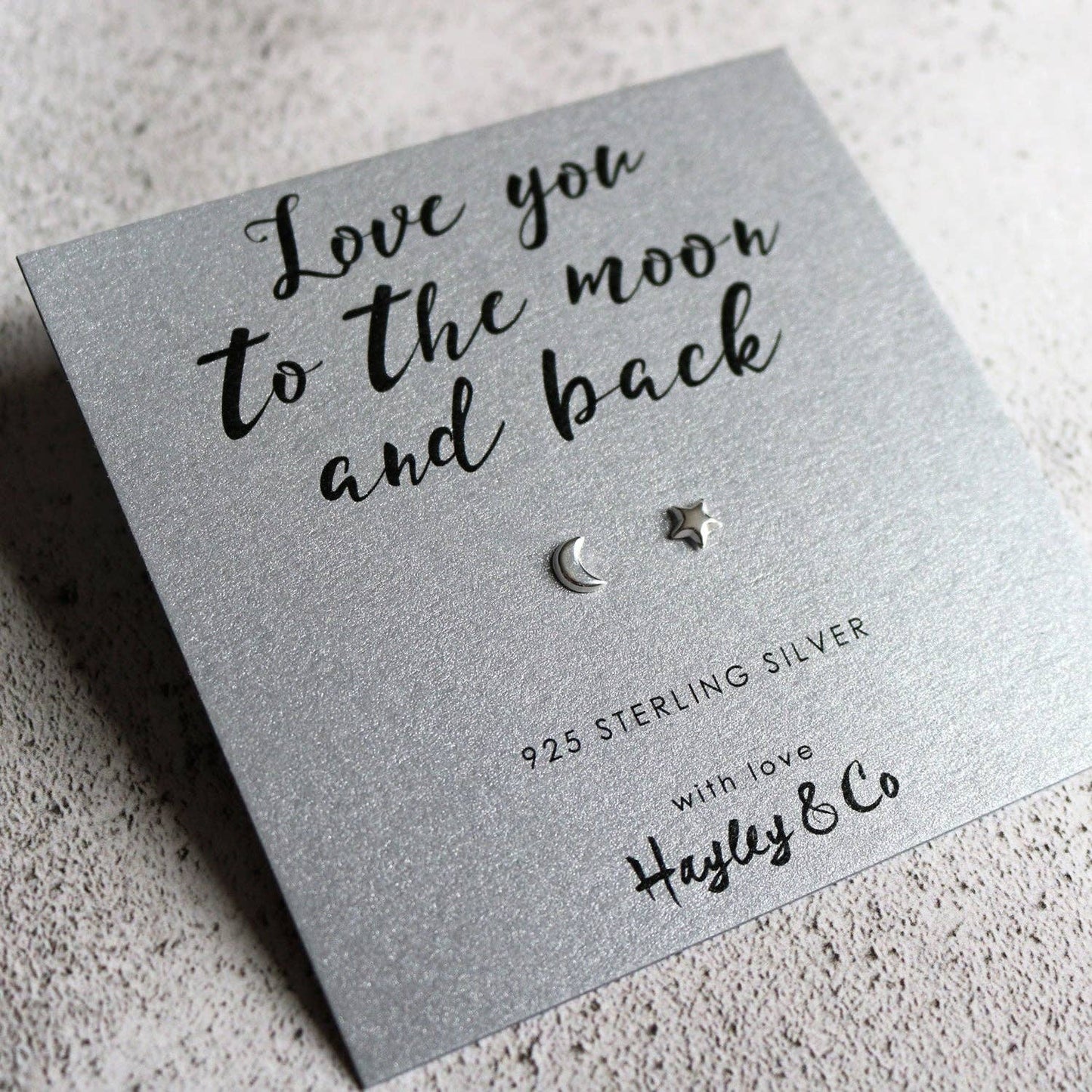 Sterling silver crescent moon and star stud earrings displayed on a textured silver gift card that reads 'Love you to the moon and back' with the brand name 'Hayley & Co'.