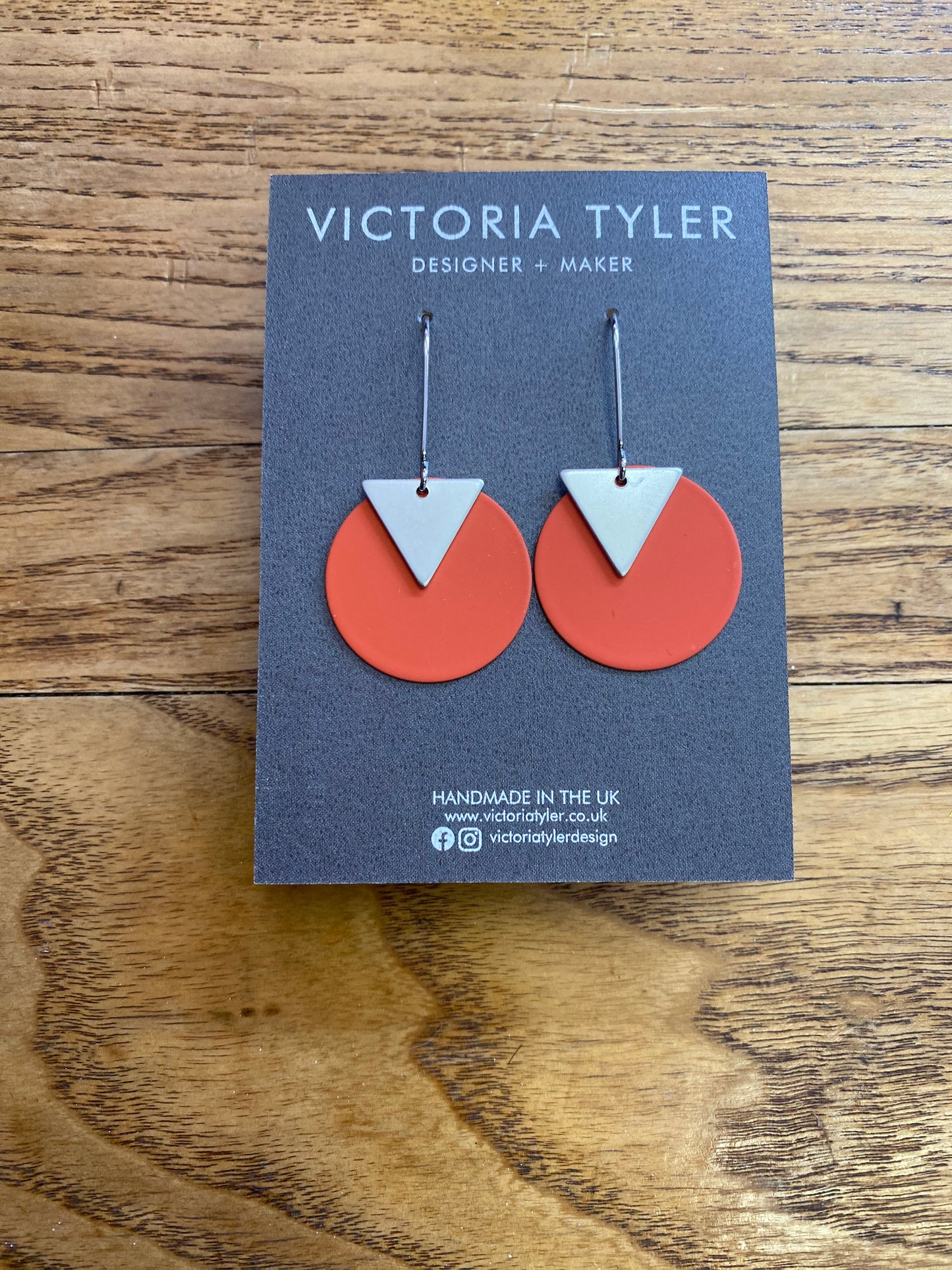 Coral coloured Circle Dangly Earrings with Silver Plate Triangles - 'Kiki'. On a black backing card which says 'Victoria Tyler, Designer + Maker